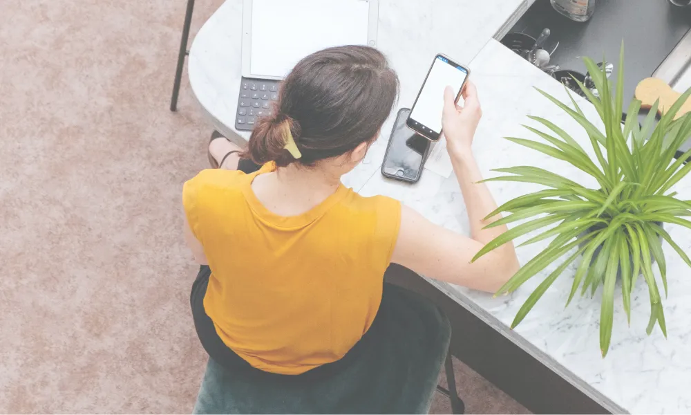 A professional woman using a phone and a tablet at a table.
