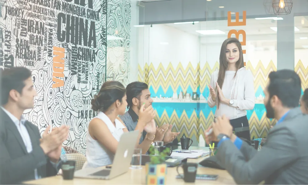 Six people gathered in a meeting room and a woman is standing up.